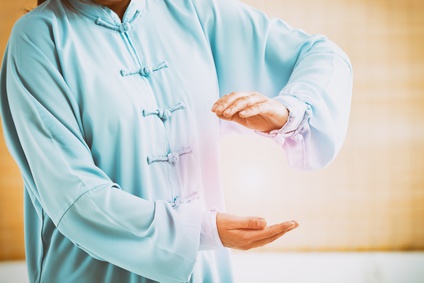 Beautiful woman doing qi gong tai chi exercise or reiki wearing professional, original Chinese clothes at gym